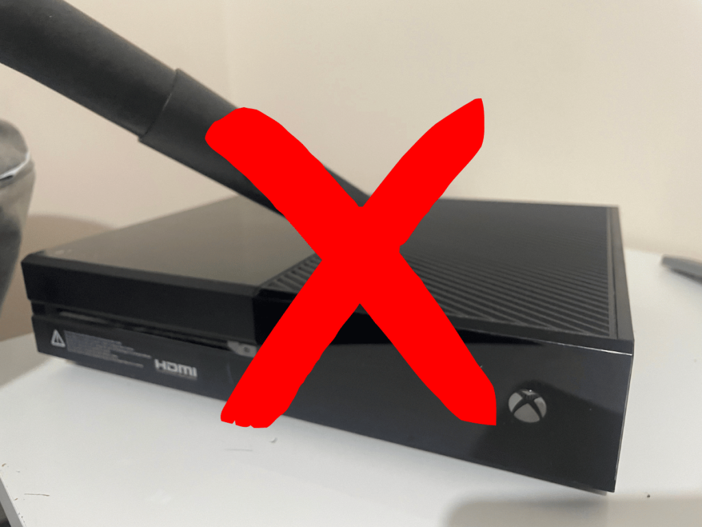 Vacuum cleaner on top of Xbox One with a cross